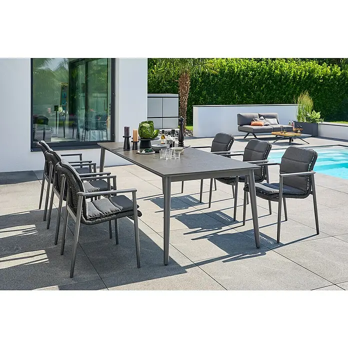 Sunfun Gartenmöbel-Set Solo Rope - 13 -tlg., Aluminium/Sintered Stone/Kunststoff/Olefin, Night-Grey, Ausziehbar - Grauer Esstisch mit sechs Stühlen im Freien. Das Set befindet sich auf einer Terrasse neben einem Pool und üppigem Grün.