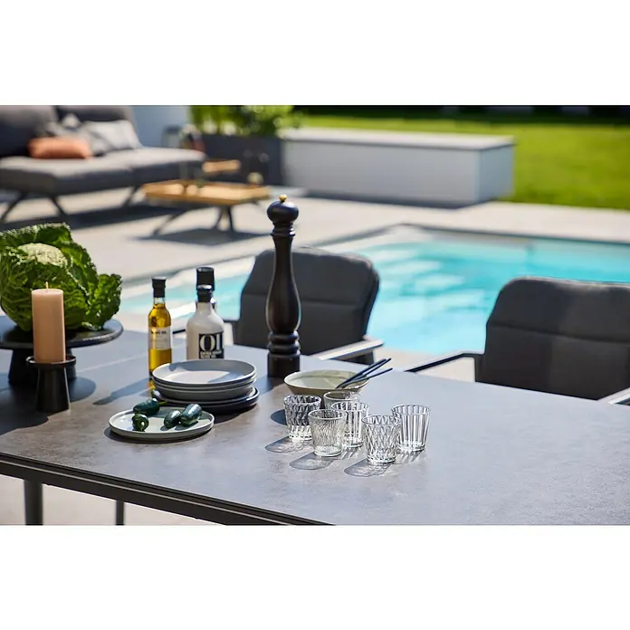 Sunfun Solo Gartentisch - L x B x H: 230 x 100 x 76,5 cm, Aluminium, Sintered Stone, Night-Grey, Ausziehbar - Ein einladender Gartentisch mit stilvollem Geschirr und Gläsern, perfekt für ein Essen im Freien mit Blick auf den Pool.