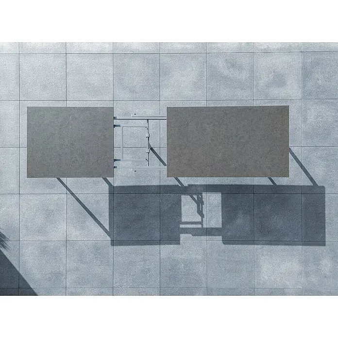 Sunfun Solo Gartentisch - L x B x H: 230 x 100 x 76,5 cm, Aluminium, Sintered Stone, Night-Grey, Ausziehbar - Draufsicht auf einen grauen Ausziehtisch mit Metallgestell auf grauem Fliesenboden, wobei die Schatten die Struktur betonen.