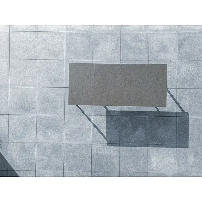 Sunfun Solo Gartentisch - L x B x H: 230 x 100 x 76,5 cm, Aluminium, Sintered Stone, Night-Grey, Ausziehbar - Ein grauer Tisch steht auf einem Fliesenboden und wirft einen Schatten. Die Oberfläche des Tisches und der Boden harmonieren gut.