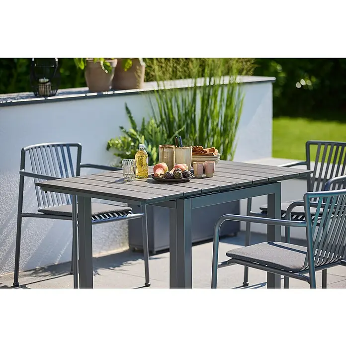Sunfun Maja Gartentisch - L x B x H: 75 x 74,5 x 75 cm, Aluminium, Polywood, Night-Grey, Ausziehbar - Ein grauer Gartentisch mit Stühlen steht auf einer Terrasse, darauf Obst, Getränke und Geschirr. Die Gartengarnitur lädt zum Verweilen im Freien ein.
