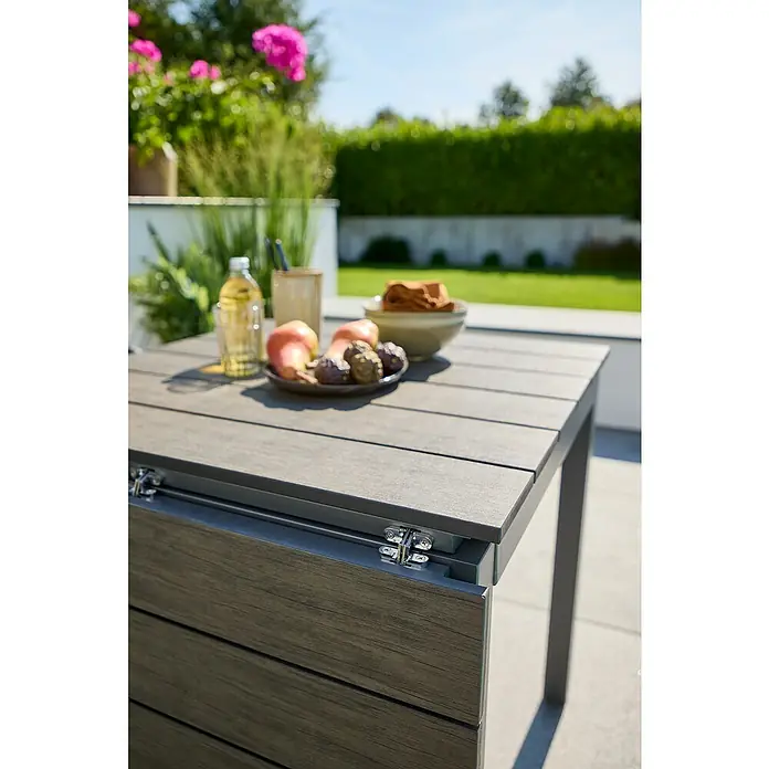 Sunfun Maja Gartentisch - L x B x H: 75 x 74,5 x 75 cm, Aluminium, Polywood, Night-Grey, Ausziehbar - Ein ausziehbarer Gartentisch aus Holz mit Früchten, Getränken und Tüchern auf einer Terrasse, perfekt für Mahlzeiten im Freien.