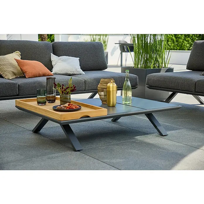 Sunfun Lumar Garten-Couchtisch - L x B x H: 120 x 80 x 27 cm, Aluminium, Night-Grey - Ein moderner Couchtisch mit Getränken und Snacks auf einer Holzablage, ergänzt das graue Gartensofa mit Kissen.