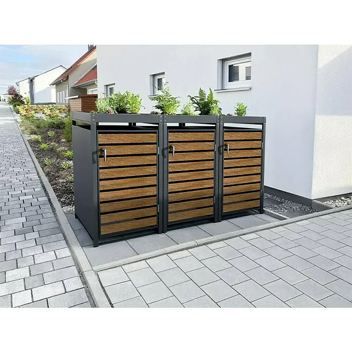 Metzler Mülltonnenbox - 204 x 80 cm, Stahl, Anthrazit/Braun, Geeignet für Anzahl Mülltonnen: 3 Stk., Mit Pflanzdach - Moderne Mülltonnenbox mit Holzverkleidung und Bepflanzung auf Pflastersteinen vor einem Haus.