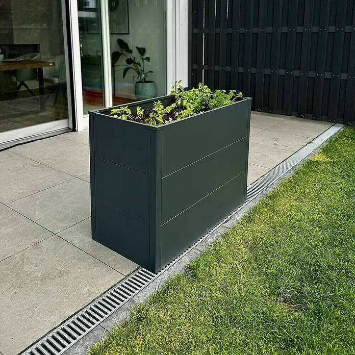 Metzler Hochbeet - 100 x 55 x 77 cm, Stahl, Anthrazit - Bild eines grauen, rechteckigen Pflanzgefäßes mit horizontalen Linien, gefüllt mit grünen Pflanzen im Freien.