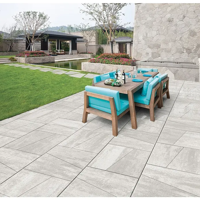 Terrassenplatte Division - 50 x 30 x 4 cm, Grau, Beton - Ein stilvoller Außenbereich mit einem Esstisch-Set auf einer grauen Steinterrasse, umgeben von einem gepflegten Garten mit Teich.