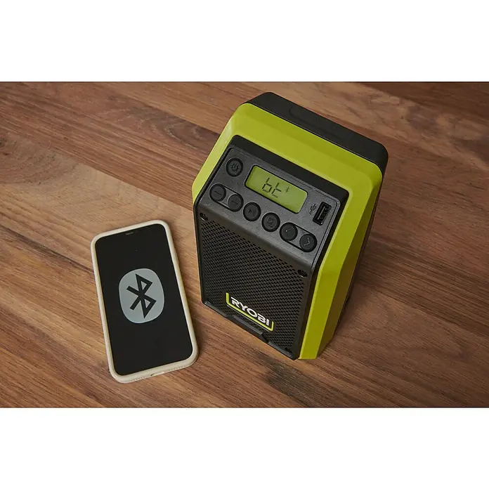 Ryobi ONE+ Akku-Bluetooth-Radio RRDAB18-0 - 10 W, Ohne Akku - Ryobi Radio und Smartphone mit Bluetooth-Symbol auf einem Holztisch. Kompakt und ideal für Baustellen.