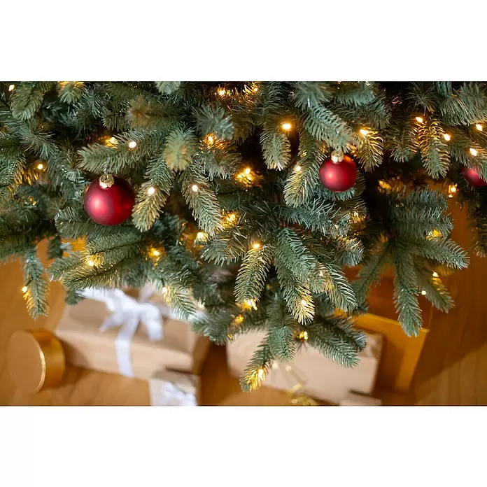Evergreen Künstlicher Weihnachtsbaum Vermont Fichte - Höhe: 240 cm, Grün, LED-Beleuchtung - Ein künstlicher grüner Weihnachtsbaum, geschmückt mit warmen Lichtern und roten Kugeln, darunter verpackte Geschenke.