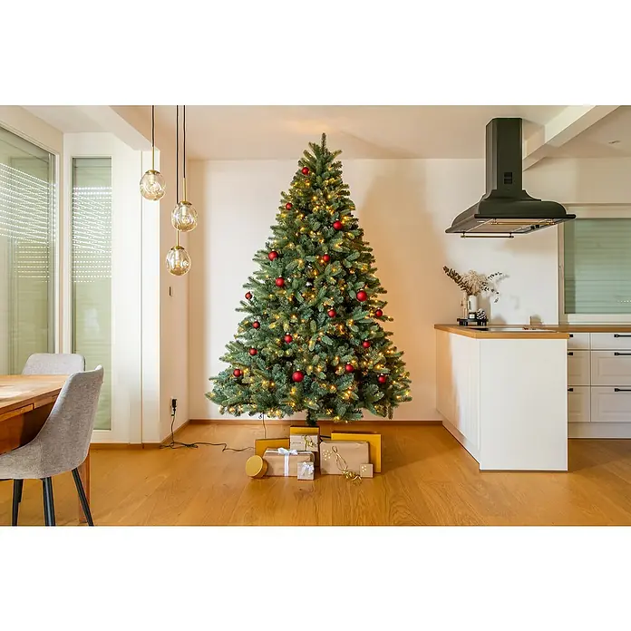 Evergreen Künstlicher Weihnachtsbaum Vermont Fichte - Höhe: 210 cm, Grün, LED-Beleuchtung - Geschmückter Weihnachtsbaum mit roten Kugeln und warmen Lichtern, umgeben von liebevoll verpackten Geschenken auf einem hellen Holzboden.