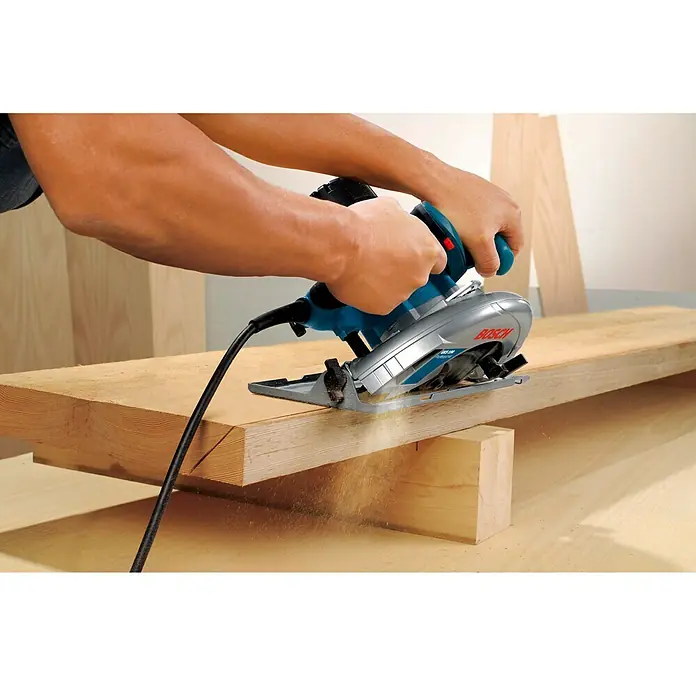 Bosch Professional Handkreissäge GKS 190 - 1.400 W, Durchmesser Sägeblatt: 190 mm, Schnitttiefe bei 90 °: 70 mm - Eine Bosch Kreissäge in Aktion, die ein Holzbrett durchschneidet. Das Werkzeug ist blau und silberfarben und scheint in gutem Zustand zu sein.