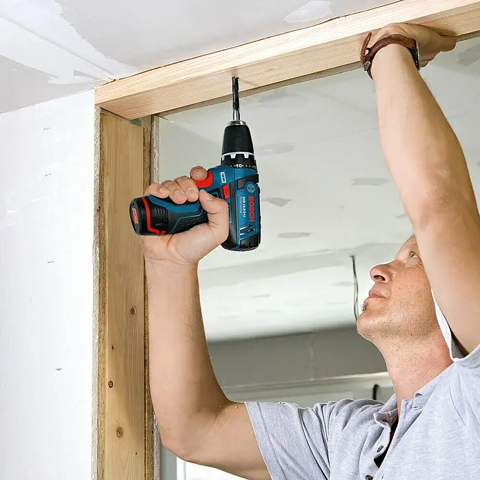 Bosch Professional Akku-Bohrschrauber GSR 12V-15 - 12 V, Ohne Akku, 30 Nm - Ein Mann, der mit einem blauen Bosch Akku-Bohrschrauber GSR 12V-15 FC arbeitet, um ein Holzstück zu befestigen.