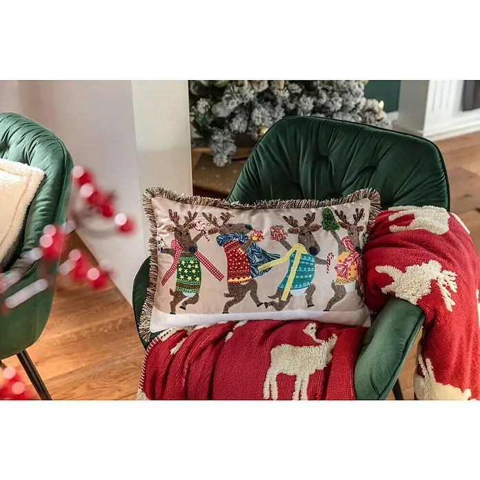 Kissen Rentiere - Weihnachten, 50 x 30 cm, 100 % Polyester - Festlicher dekorativer Akzent: Ein rechteckiges Kissen mit einem verspielten Rentierdesign, perfekt für die Weihnachtszeit, liegt auf einem grünen Sessel.
