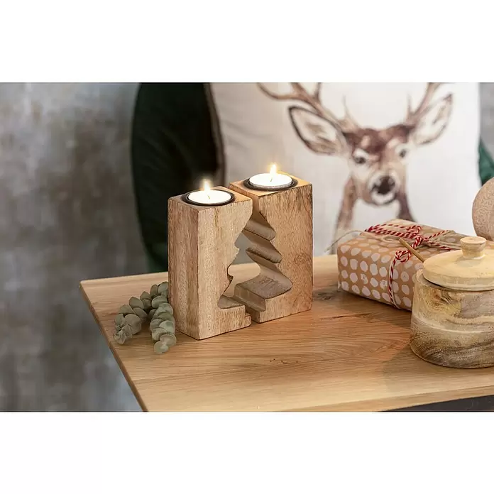 Kissen Hirsch - Braun, 45 x 45 cm, 100 % Polyester - Zwei Holz-Teelichthalter mit brennenden Kerzen, einer mit Tannenbaum-Ausschnitt, auf einem Holztisch mit festlicher Dekoration.