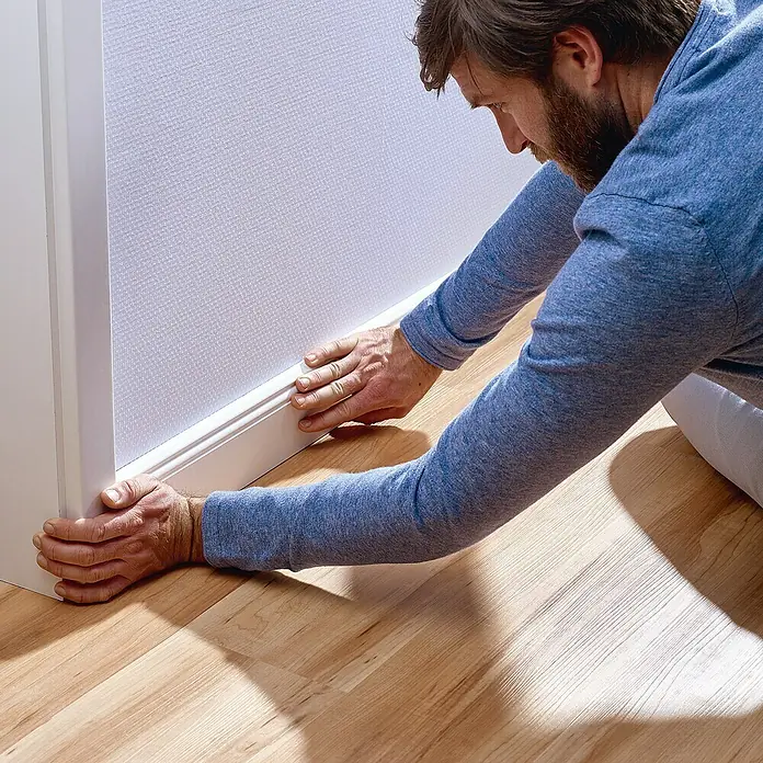 Tesa Montageband - Geeignet für: Tapeten, Belastbarkeit pro m: 10 kg, 1,5 m x 19 mm - Mann, der weiße Sockelleisten an einer Wand anbringt, um die Inneneinrichtung des Raumes zu vervollständigen.