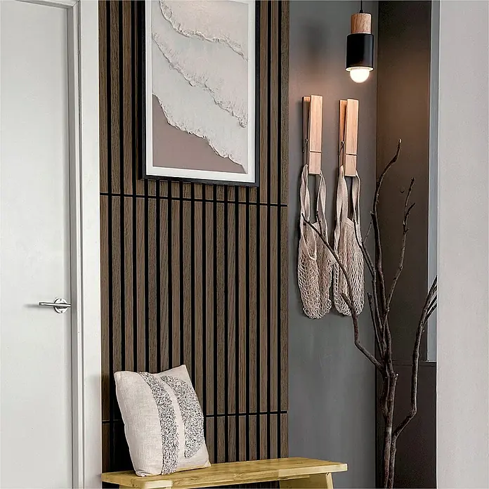 acous Akustikpaneel Compact - Eiche dunkel, L x B x S: 2.440 x 305 x 10,3 mm, 2 Stk. - Nahaufnahme einer stilvollen Inneneinrichtung mit einer Akzentwand aus Holzlatten, einem abstrakten Gemälde, einer Pendelleuchte und dekorativen Netztaschen.