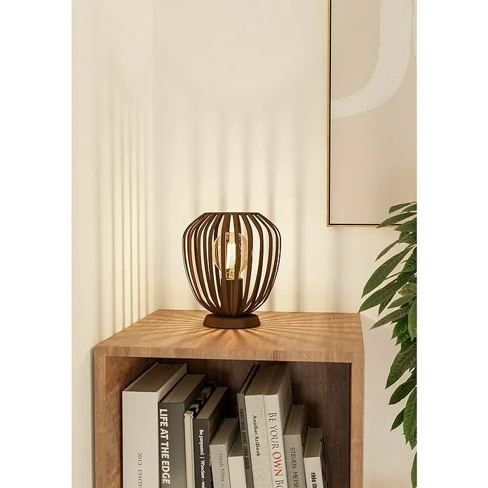Eglo Lámpara de sobremesa Espinal - E27, Ancho: 19,5 cm, Potencia por luz: 40 W - Una lámpara de mesa de celosía marrón con una bombilla se encuentra sobre una mesa de madera junto a libros, creando un ambiente acogedor.