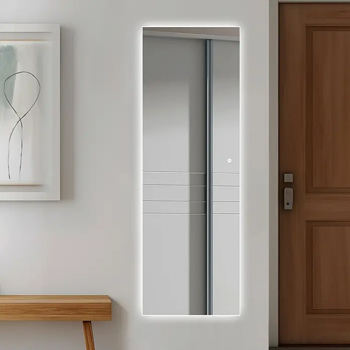 Espejo con luz Shira Home - 50 x 150 cm, Sensor - Un espejo rectangular iluminado con LED cuelga en una pared, al lado de una puerta de madera y una pequeña mesa de madera.
