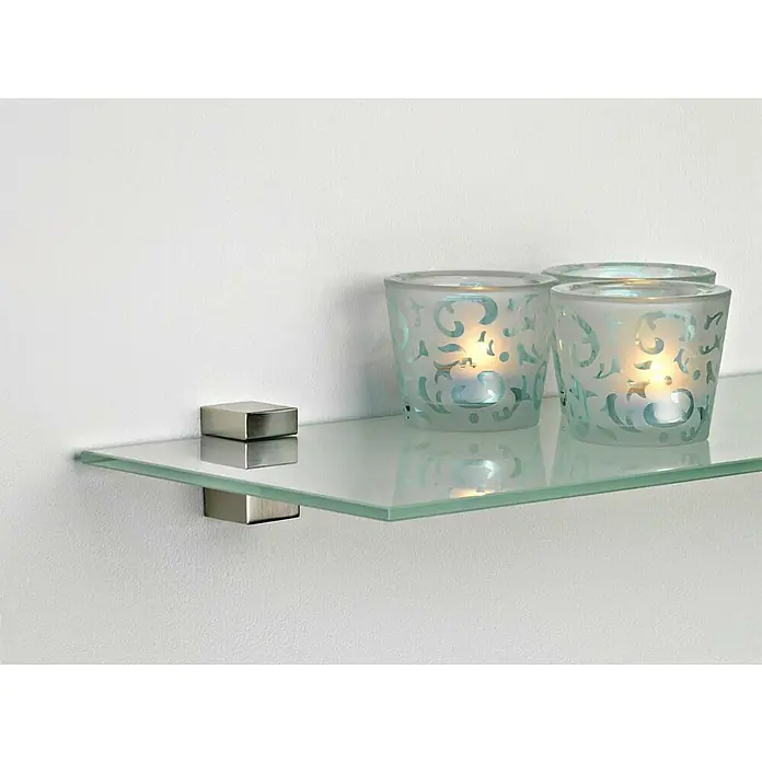 Rei Soporte de pared para estantes 2440 - Carga soportada: 20 kg, Apto para: Estantes, Cromo, Mate, 2 ud. - Una estantería de vidrio con soportes en una pared blanca, mostrando tres portavelas decorativos con velas encendidas.