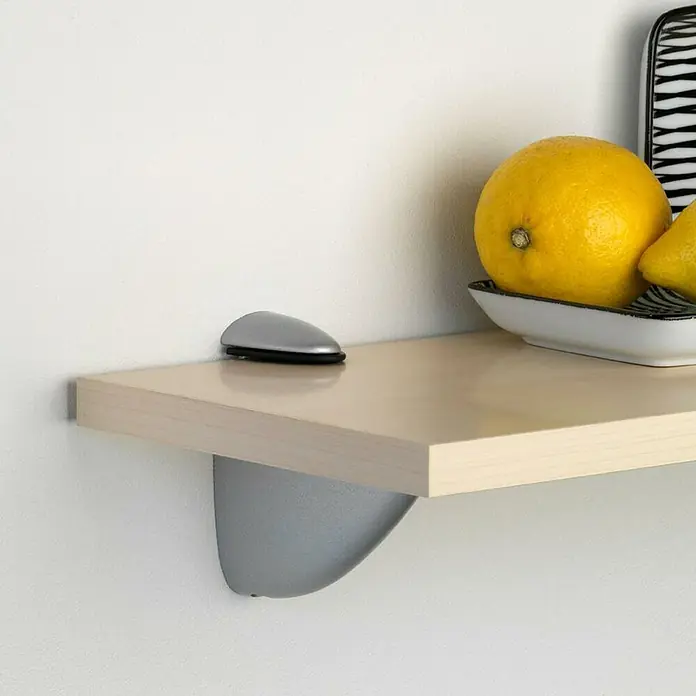 Rei Soporte de pared para estantes Pelican - L x An x Al: 8,9 x 10,6 x 4 cm, Cromo, Apto para: Estantes - Primer plano de una estantería flotante con soporte plateado, mostrando un cuenco de limones y un alfombrilla de ratón.