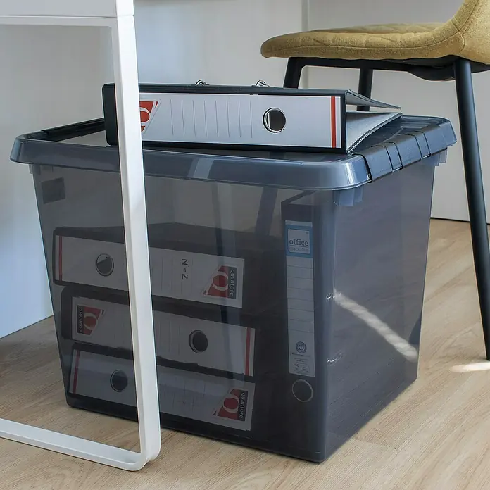 Sunware Aufbewahrungsbox Comfort Line - L x B x H: 50 x 40 x 38 cm, Transparent grau, Kunststoff - Ein grauer Aufbewahrungsbehälter aus Kunststoff mit Aktenordnern, mit einem weiteren Ordner obendrauf, steht unter einem Tisch und einem Stuhl.