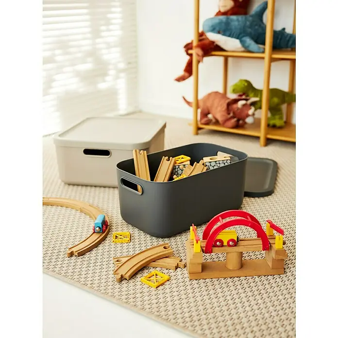 Rotho Aufbewahrungsbox - L x B x H: 39,5 x 35,5 x 17,7 cm, Kunststoff, Anthrazit, 20 l - Aufnahme von zwei grauen und beigen Spielzeugkisten auf einem Teppich, wobei die graue Kiste mit Holzspielzeug gefüllt ist.