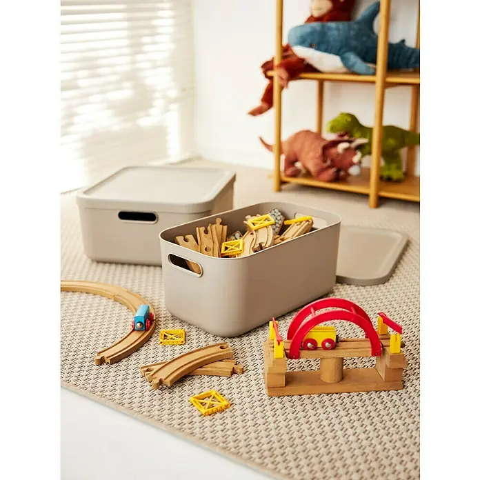 Rotho Aufbewahrungsbox - L x B x H: 39,2 x 35,5 x 17,7 cm, Kunststoff, Cappuccino, 20 l - Bild von zwei grauen Aufbewahrungsboxen mit Deckel und Holzspielzeug wie Zugschienen und einer Brücke auf einem Teppich.