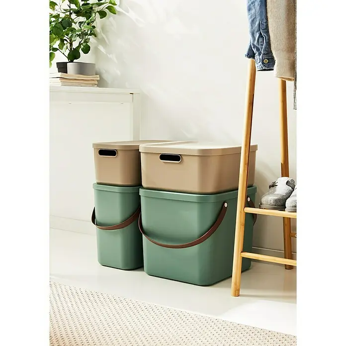 Rotho Aufbewahrungsbox - L x B x H: 39,2 x 35,5 x 17,7 cm, Kunststoff, Cappuccino, 20 l - Zwei grüne Aufbewahrungskörbe mit braunen Henkeln und beigefarbenen Deckeln stehen auf einem gemusterten Teppich.