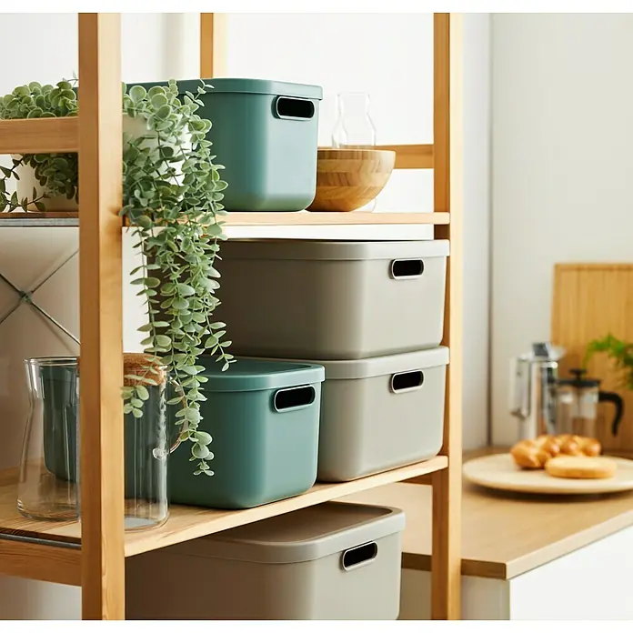 Rotho Aufbewahrungsbox - L x B x H: 39,2 x 23,5 x 17,7 cm, Kunststoff, Mistelzweiggrün, 12 l - Auf einem Holzregal sind mehrere dekorative Aufbewahrungsboxen in Grün- und Grautönen gestapelt.