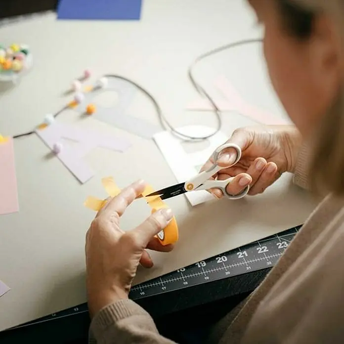 Fiskars Tijeras para manualidades Micro-Tip - Largo: 12,3 cm, Longitud de corte: 4,7 cm, Acero inoxidable - Una persona usa tijeras Fiskars para cortar papel amarillo, creando decoraciones coloridas. Manualidades y creatividad con tijeras de calidad.