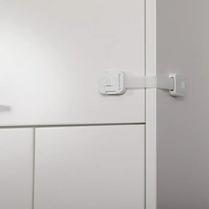 Dreambaby Multifunktionsverschluss - Kleben, 2 Stk. - Das Bild zeigt einen weißen DreamBaby Schrankschloss, das an einer weißen Kommode befestigt ist, um Kinder vor dem Öffnen zu schützen.