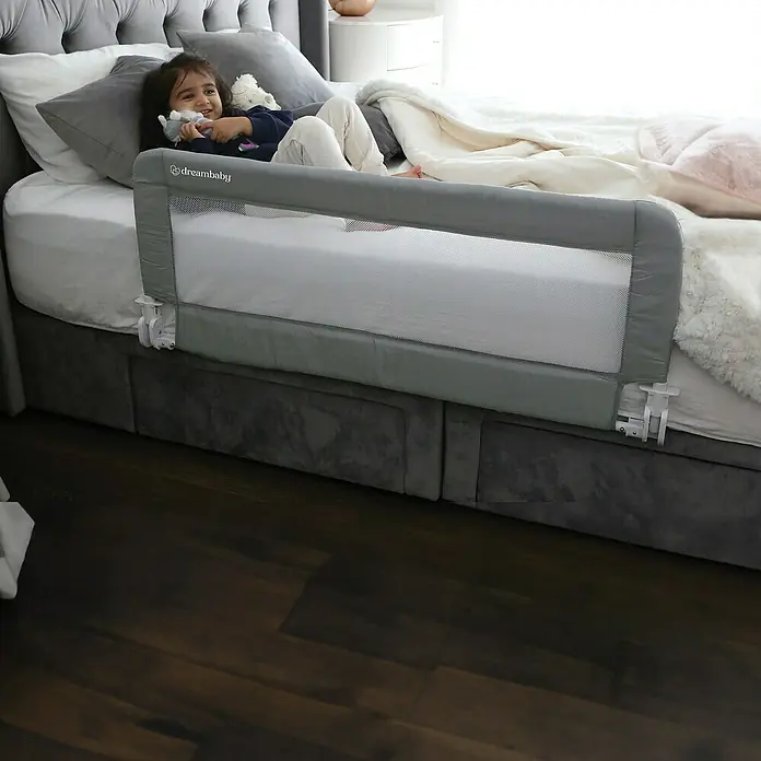 Dreambaby Bettgitter Milan - L x H: 110 x 45 cm, Grau - Kind liegt in einem Bett mit einem grauen Dream Baby Bettschutzgitter.