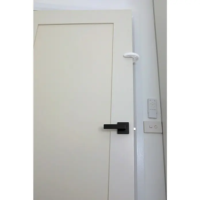Dreambaby Fingerschutz - Weiß, 1 Stk. - Ein weißer Türanschlag ist an der Oberseite einer weißen Tür befestigt, um zu verhindern, dass sie an die Wand stößt.