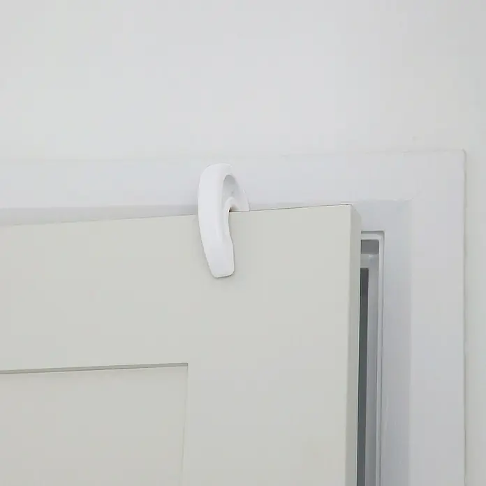 Dreambaby Fingerschutz - Weiß, 1 Stk. - Nahaufnahme eines weißen, gebogenen Türhakens, der über eine graue Schranktür gehängt ist, mit weißem Rahmen im Hintergrund.