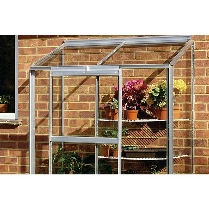 Halls Gewächshaus Altan 2 - Außenmaß inkl. Dachüberstand (B x T): 68 x 131 cm, Material Seitenwand: Glas, 3 mm, Silbergrau - Nahaufnahme eines Gewächshauses mit Pflanzen, das an einer Ziegelmauer steht und für den Pflanzenanbau genutzt wird.