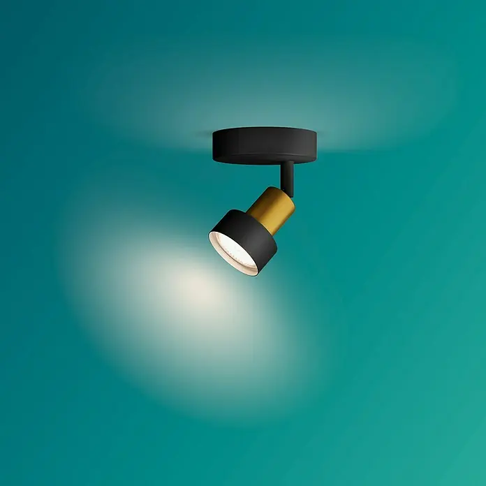 Philips Foco de pared Conduit - 5 W, 11 x 10 x 9 cm, Negro, GU10 - Primer plano de una lámpara de techo giratoria negra y dorada, que emana un brillo cálido en una habitación con un fondo azul verdoso.
