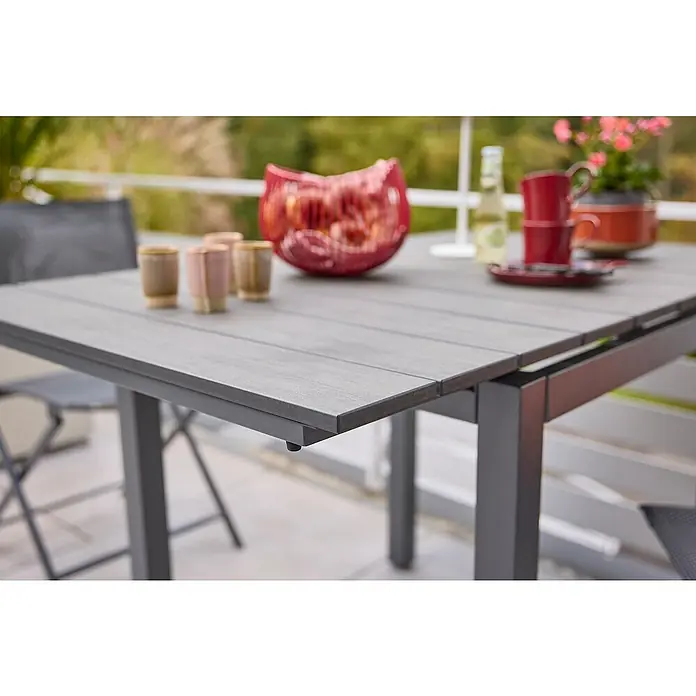 Sunfun Maja Gartentisch - L x B x H: 75 x 74,5 x 75 cm, Aluminium, Polywood, Night-Grey, Ausziehbar - Nahaufnahme eines Gartentisches mit grauer Tischplatte und Metallgestell, dekoriert mit Vasen, Tassen und einer Pflanze.