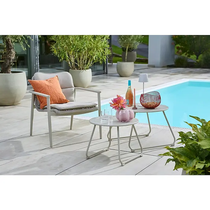 Sunfun Loungemöbel-Set Solo Rope/Sarah - 4 -tlg., Aluminium/Polyrattan/Stahl, Light-Greige - Ein grauer Gartensessel mit Kissen und zwei Beistelltischen auf einer Terrasse neben einem Pool. Ideal zum Entspannen im Freien.