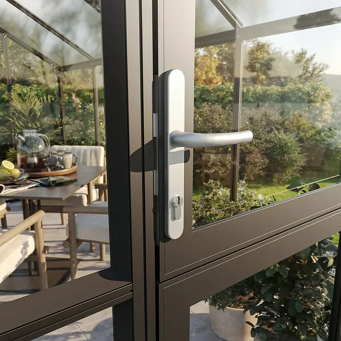 KGT Gewächshaus Galant III - Außenmaß inkl. Dachüberstand (B x T): 216 x 308 cm, Material Seitenwand: Glas, 4 mm, Tannengrün - Nahaufnahme eines eleganten Türgriffs an einer Terrassentür, die in einen üppigen Garten führt. Der Griff ist aus gebürstetem Stahl und wirkt modern.