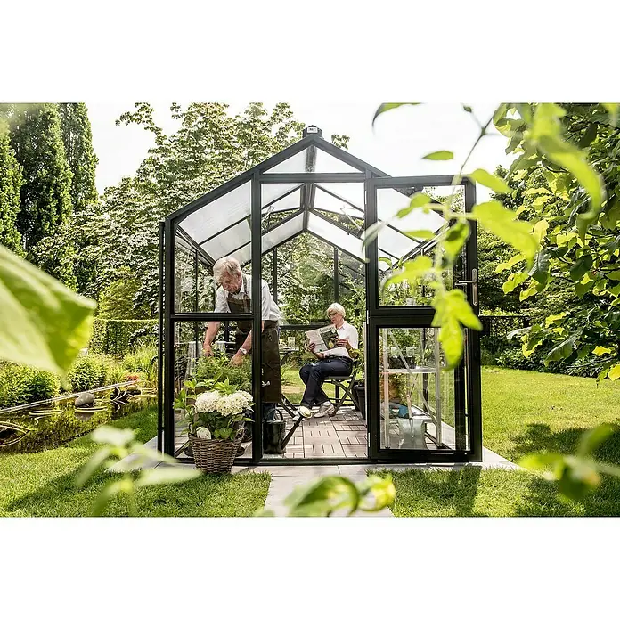 KGT Gewächshaus Galant III - Außenmaß inkl. Dachüberstand (B x T): 216 x 308 cm, Material Seitenwand: Glas, 4 mm, Tannengrün - Gartenszene mit Gewächshaus: Ein Paar genießt die Gartenarbeit und entspannt sich. Das Gewächshaus bietet einen idealen Raum für Pflanzen und Erholung.