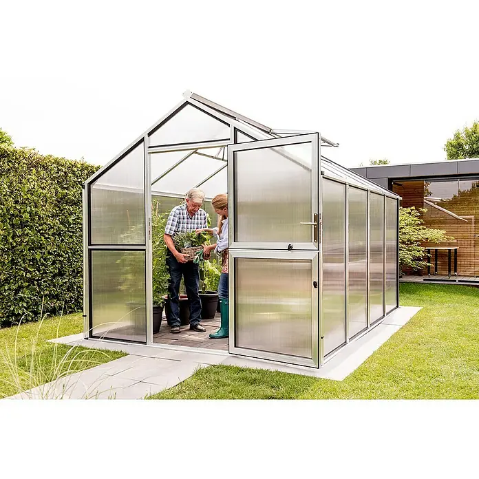KGT Gewächshaus Novum IV - Außenmaß inkl. Dachüberstand (B x T): 273 x 408 cm, Material Seitenwand: Kunststoff, 10 mm, Pressblank - Ein Gewächshaus aus Metall mit einer geöffneten Tür, durch die ein älterer Mann und eine jüngere Frau mit einer Ernte aus dem Garten gehen.