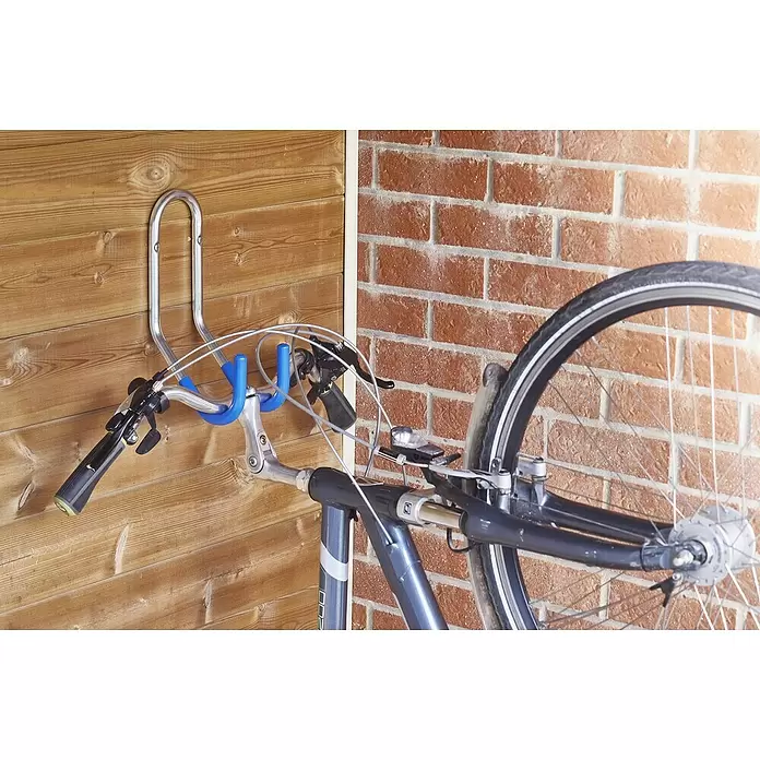 Mottez Gancho de pared para bicicletas - Diámetro: 16 mm, Acero, Plateado - Soporte de pared plateado para bicicleta con fundas azules, sujetando una bicicleta gris por el manillar, sobre pared de madera y ladrillo.