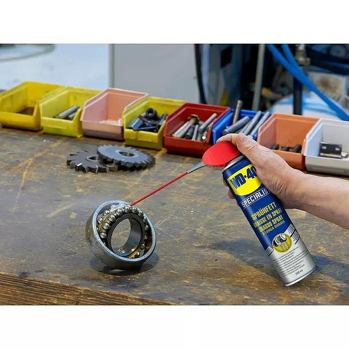 WD-40 Specialist Ketten-Sprühfett - 300 ml - Hand sprüht WD-40 Specialist Sprühfett auf ein Kugellager auf einer Werkbank.