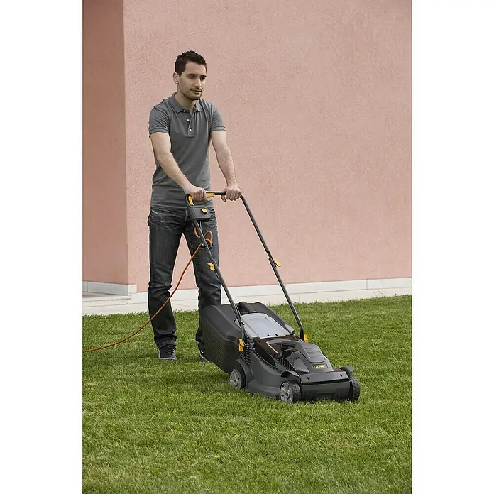 Alpina Cortacésped eléctrico BL320E - 1.000 W, Ancho de corte: 32 cm - Un hombre está cortando el césped con un cortacésped Alpina frente a un edificio rosa.
