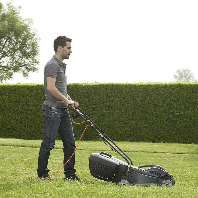 Alpina Cortacésped eléctrico BL320E - 1.000 W, Ancho de corte: 32 cm - Un hombre está cortando el césped con una cortadora de césped negra con un cable naranja en un jardín verde.