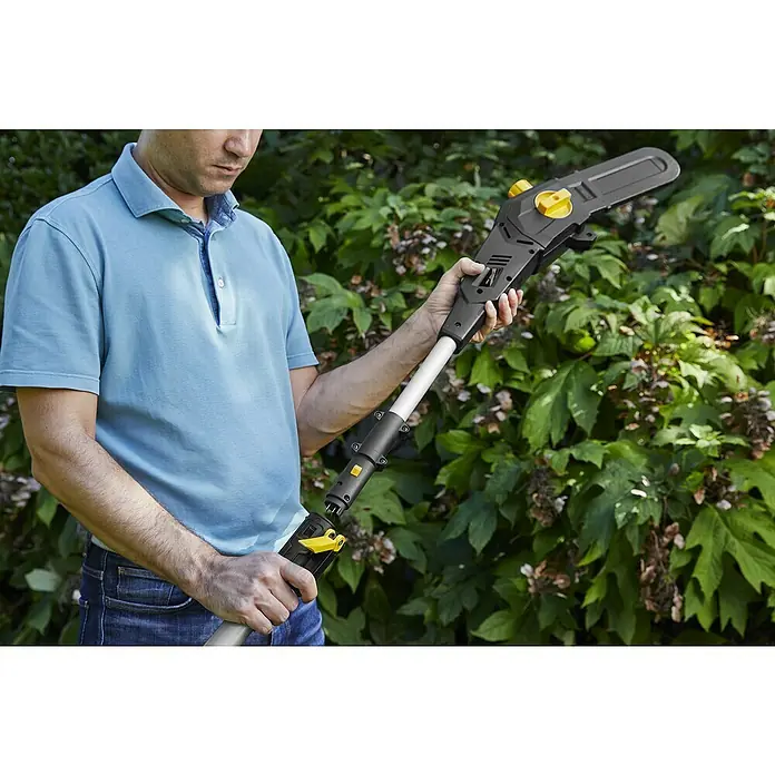 Alpina Multiherramienta de batería AM20 - 20 V, 1 batería, 4 Ah - Un hombre ensambla una motosierra eléctrica de pértiga en el jardín para podar árboles y arbustos, con detalles amarillos.
