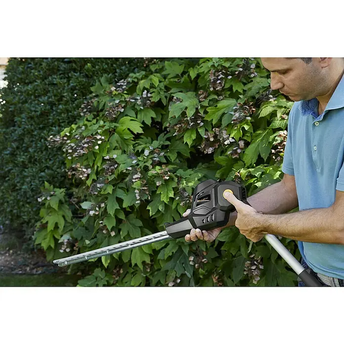 Alpina Multiherramienta de batería AM20 - 20 V, 1 batería, 4 Ah - Un hombre está operando un cortasetos Worx contra un arbusto verde.