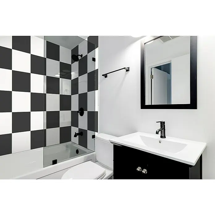 Feinsteinzeugfliese Barcelona Negro - 24,8 x 24,8 cm, Schwarz, Matt - Helles Badezimmer mit schwarz-weiß karierten Fliesen in der Dusche, einem schwarzen Waschtischunterschrank und einem passenden Spiegel.