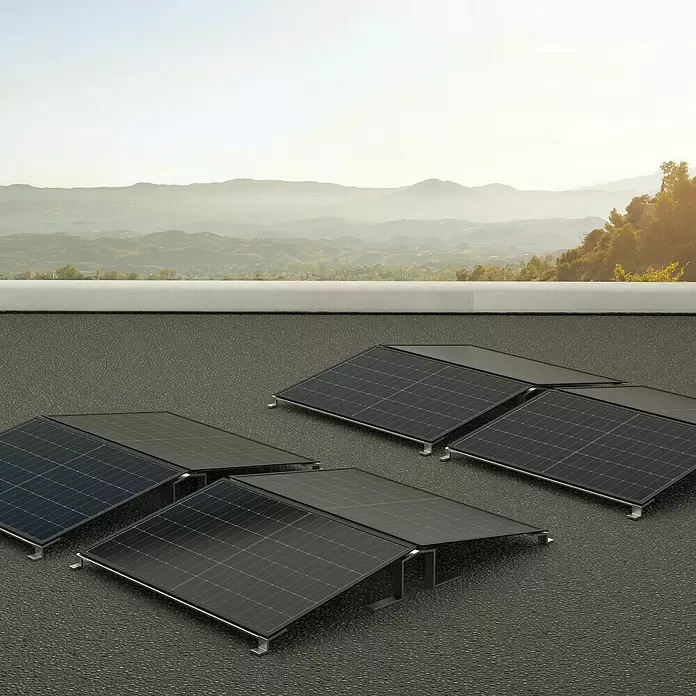 Green Solar Befestigungs-Set - Passend für: 24 Solarmodule, Geeignet für: Flachdach - Schwarze Solarmodule mit Metallstützen auf einem Dach, mit Bergen im Hintergrund.