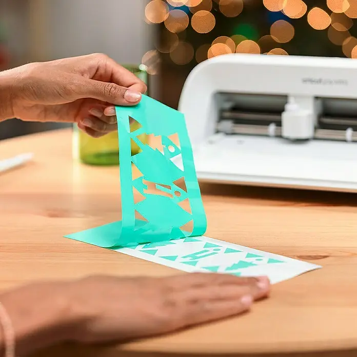 Cricut Maker Schneideplotter Maker 3 - Blau, Bluetooth, Schnittbreite: 29,7 cm, Schnittlänge: 3,6 m - Nahaufnahme einer Person, die überschüssiges Vinyl von einem individuell geschnittenen Design mit einem Cricut Schneideplotter entfernt.
