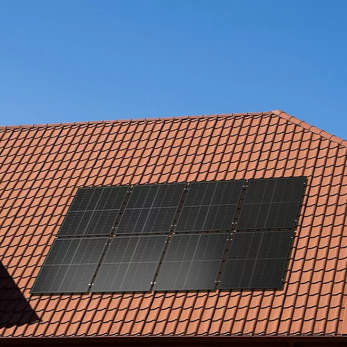 Green Solar Befestigungs-Set - Passend für: 10 Solarmodule, Geeignet für: Schrägdach - Schwarze Solarmodule auf einem roten Ziegeldach unter klarem blauem Himmel.